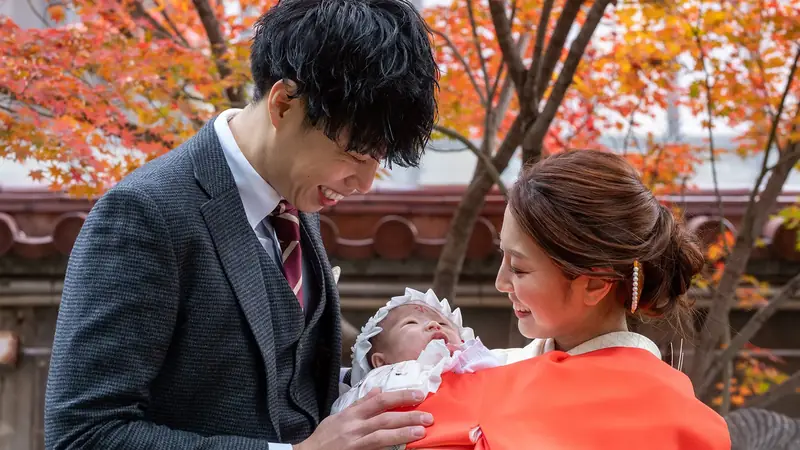 紅葉を背景に赤ちゃんを抱くお母さんと見守るお父さん