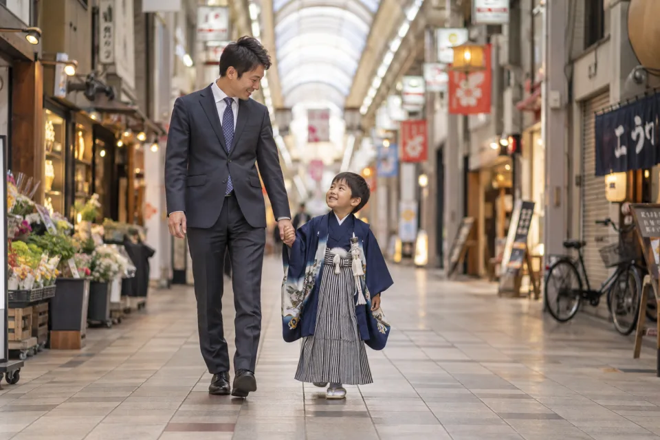 七五三の羽織袴を着た男の子とお父さんが、手をつないで商店街を歩く撮影イメージ