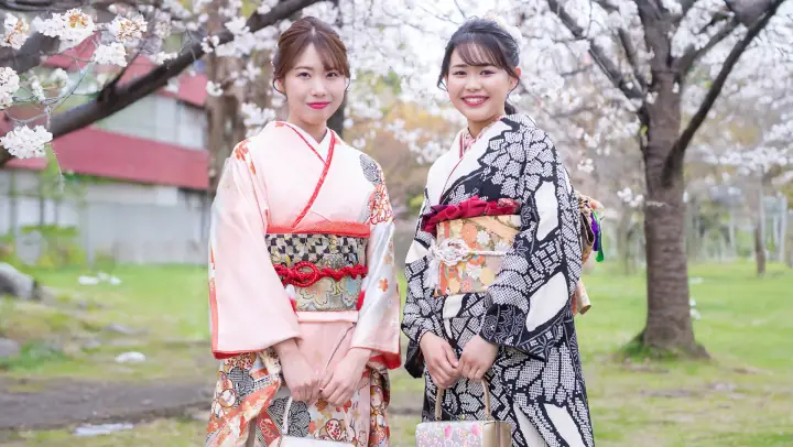 満開の桜の下で並んで立つ振袖姿の女性2人